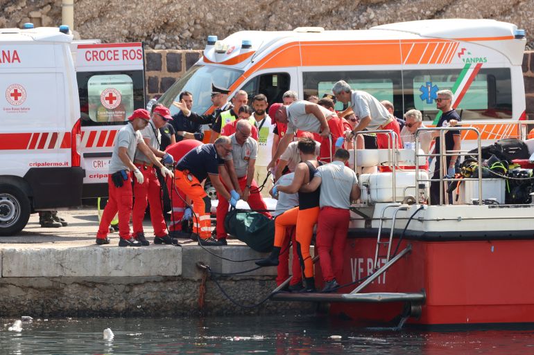 Emergency services carry a body bag after a sailboat sank in the early hours of Monday, off the coast of Porticello, near the Sicilian city of Palermo, Italy