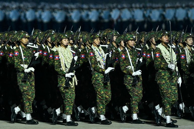 Myanmar soldiers march in their parade. They are carrying weapons and some have multiple flower garlands around their necks