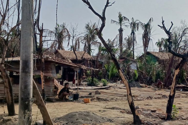 A woman cooking next to destroyed houses and trees in a Rakhine village.