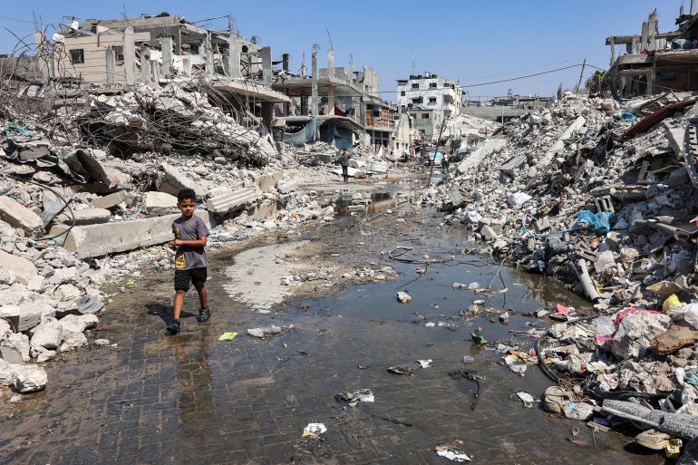 A boy walks through a puddle of sewage water past mounds of trash and rubble along a street in the Jabalia camp for Palestinian refugees in the northern Gaza Strip on August 14, 2024 amid the ongoing conflict in the Palestinian territory between Israel and Hamas. (Photo by Omar AL-QATTAA / AFP)