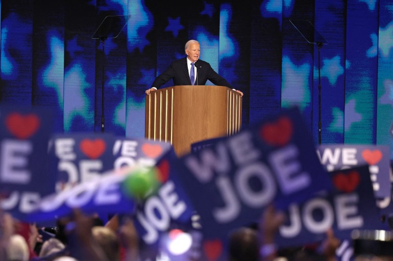 a man stands at a podium in front of signs saying we love Joe